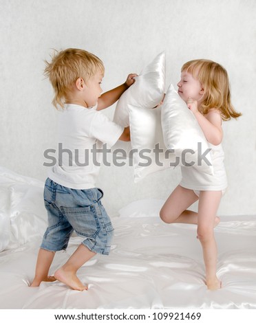 happy laughing brother and sister  having a pillow fight in bed at home