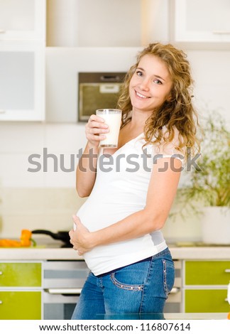 Pregnant mother drinks the milk on the house kitchen. Looking at camera