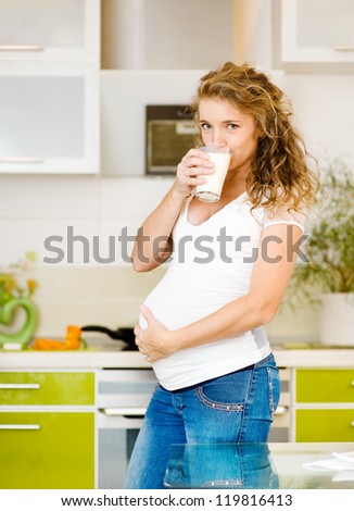 Beautiful pregnant mother drink milk. stand on the house kitchen