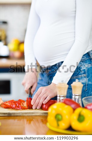 Close up pregnant woman with knife on kitchen cuts vegetables