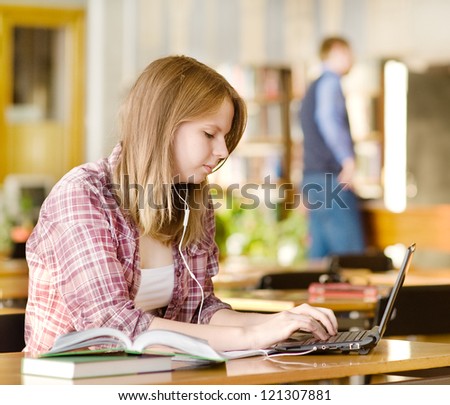 pretty female student with laptop and books working in a high school library