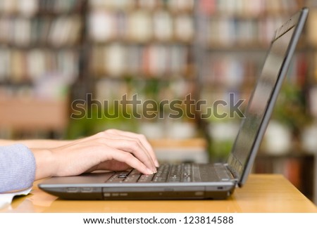 Hands typing on notebook in library