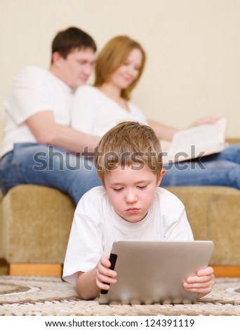 the boy plays on a tablet computer near parents reading the book