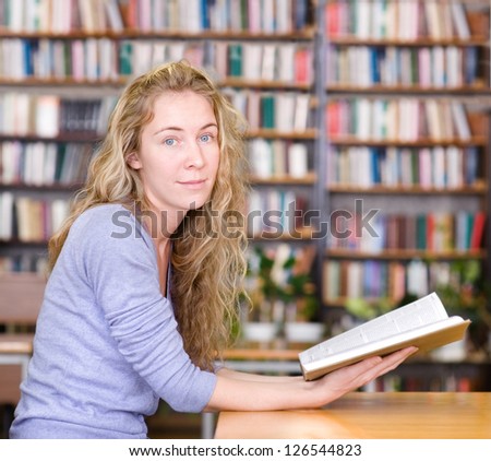 female student reads the book in library. looking at camera