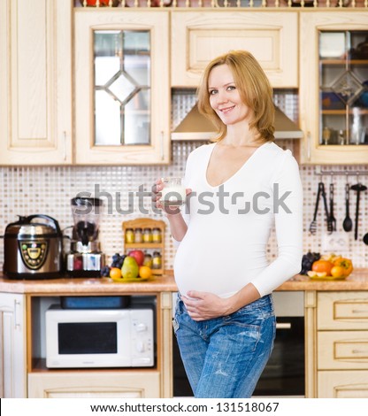 Pregnant mother drinks the milk on the house kitchen. Looking at camera