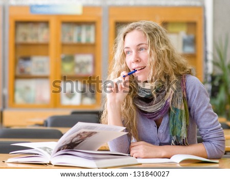 female student reads the book in library. looking away