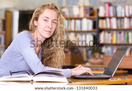 female student with laptop working in library. looking at camera