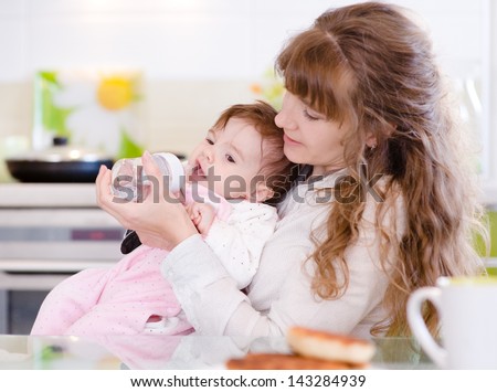 Mother feeding baby with feeding bottle in kitchen