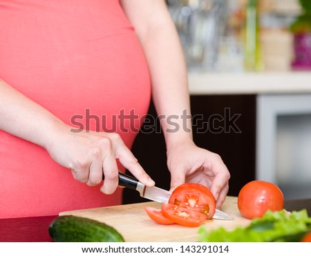 Close up pregnant woman with knife on kitchen cuts tomato