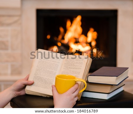 hands holding open book and cup of coffee near the fireplace