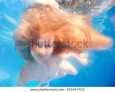Swimming young girl with long haired underwater in pool