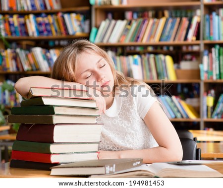 the tired student sleeps in library on pile books