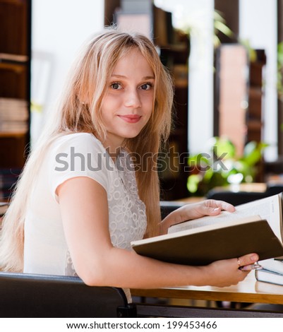Portrait of a pretty female student studying in library with open book