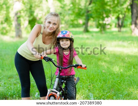 portrait of a happy mother embracing daughter who learns to ride a bike
