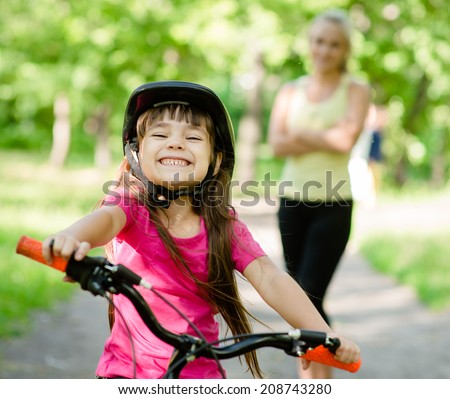 Portrait of a little girl riding her bike ahead of her mother