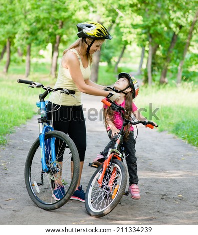 young mother dresses her daughter\'s bicycle helmet