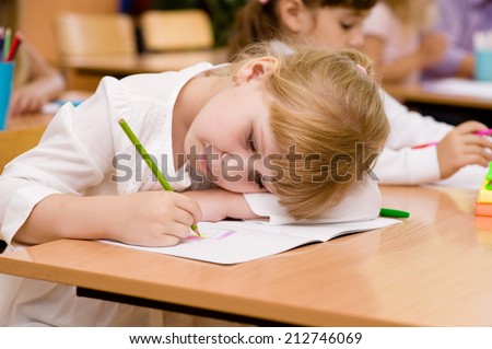 tired schoolgirl writes in a notebook during lesson