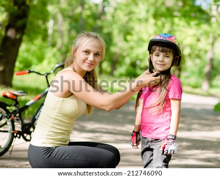 young mother dresses her daughter\'s bicycle helmet