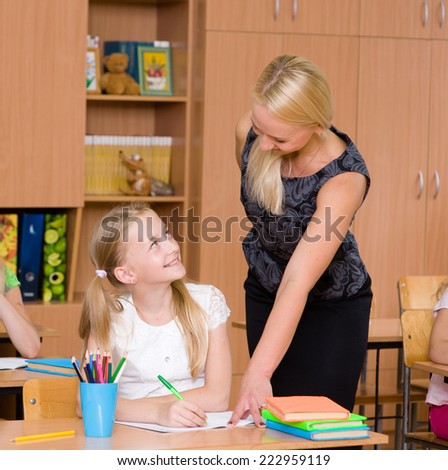 caring elementary school teacher helping student in classroom