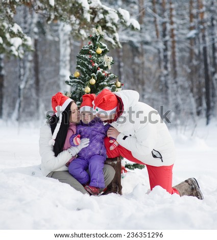 Mom and Dad kissing daughter near a Christmas tree in winter forest