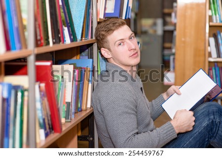 Male student with book sitting on floor in library