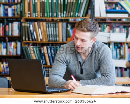 Male student with laptop studying in the university library