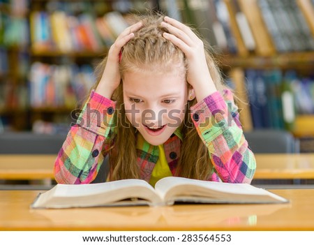 Surprised girl reading a book in the library