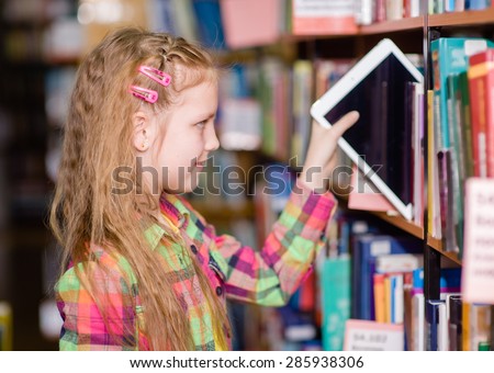 Happy teen girl pulls a tablet pc off the shelves in the library
