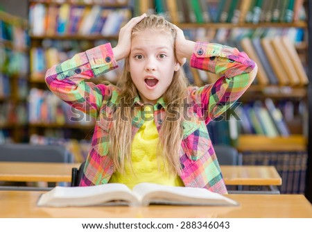 Surprised girl reading a book in the library