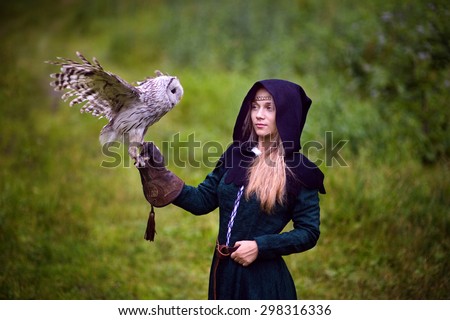 girl in medieval dress is holding an owl on her arm