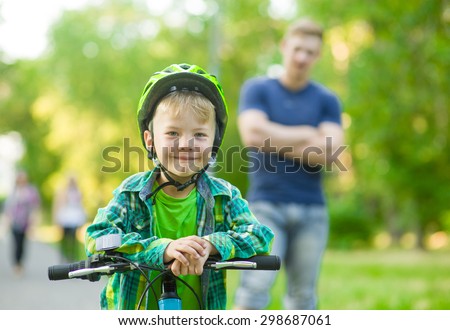 child on a bicycle with father in the park