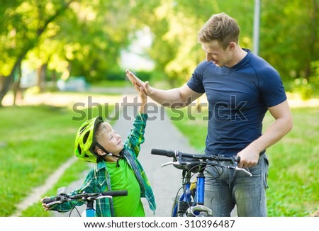 father and son give high five while cycling in the park