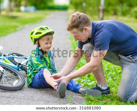 father putting band-aid on young boy\'s injury who fell off his bicycle.