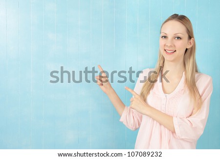 Half body portrait of beautiful young woman smiling and pointing with blue tiled background and copy space.
