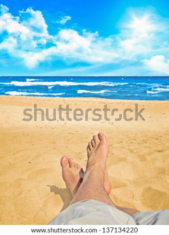 Feet of a relaxing person on a sandy beach at the ocean