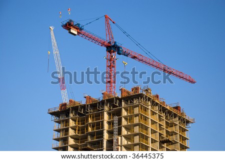 Highrise building construction site with tower cranes above it.
