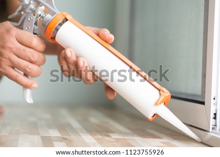 Men\'s hand uses silicone adhesive with a glue gun to repair worn windows.