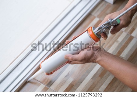 Men's hand uses silicone adhesive with a glue gun to repair worn windows.