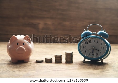 Piggy bank, stack of coins and alarm clock on wooden table. Time to invest your savings