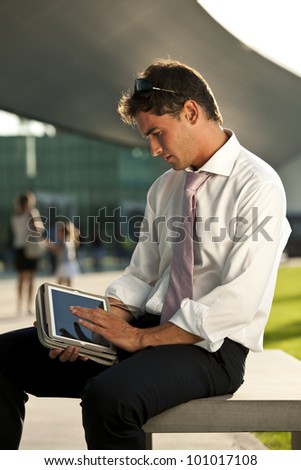 Relaxed businessman using his PC tablet while sitting on a bench