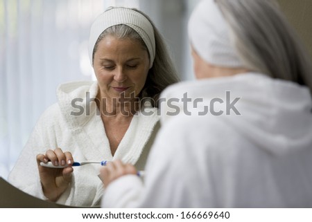 Senior woman brushing her teeths in front of the mirror