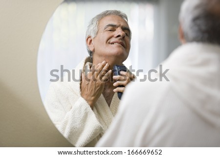 Senior happy man shaving his in front of the mirror
