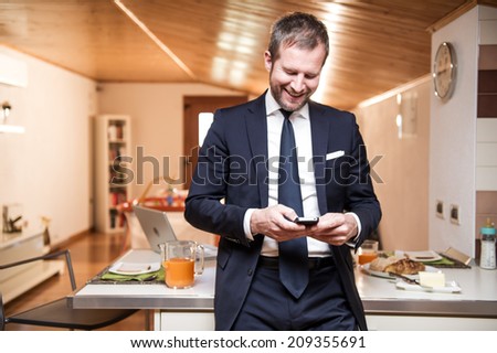 Young businessman using his mobile phone at home during breakfast