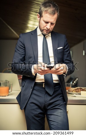 Young businessman using his mobile phone at home during breakfast