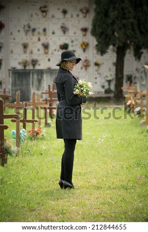 Woman standing at cemetery holding flowers