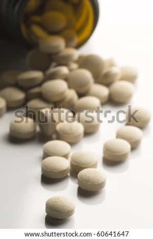 White tablets, pills,  spilled from a prescription bottle isolated on white, selective focus