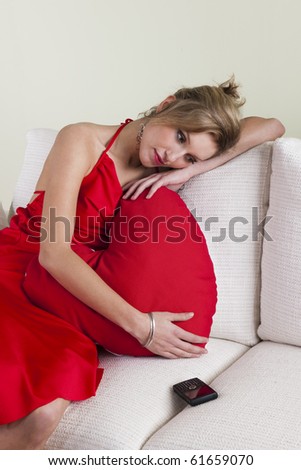 Sad and disappointed woman waiting a call, embracing a heart shaped  cushion