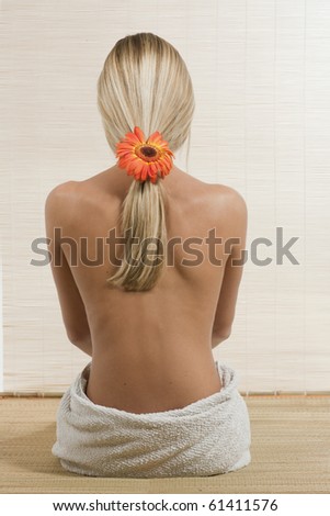 Back of woman with flower in her blond hair, sitting on a bamboo mat