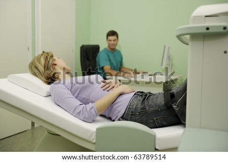 Young woman receiving MRI scan to her leg, while doctor checking results on the monitor