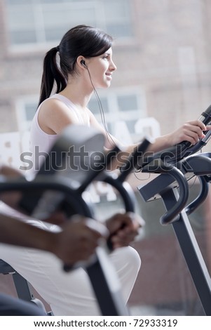 Young woman on bike at gym, exercising and listening to music